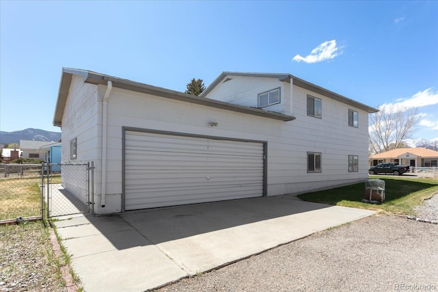 view of property exterior featuring driveway, a gate, fence, a mountain view, and an attached garage