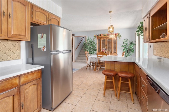 kitchen featuring decorative backsplash, appliances with stainless steel finishes, light countertops, light tile patterned floors, and a peninsula