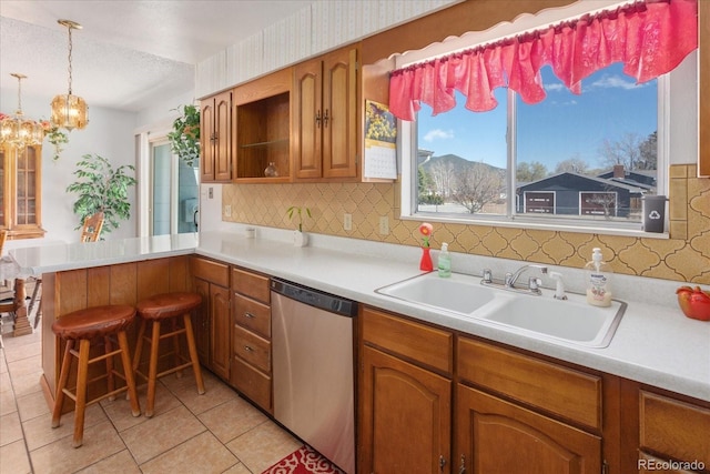 kitchen with stainless steel dishwasher, brown cabinets, a sink, light countertops, and a peninsula