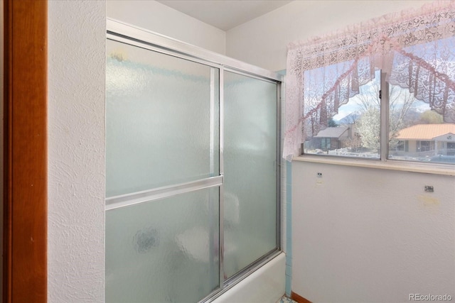 full bathroom with a textured wall and shower / bath combination with glass door