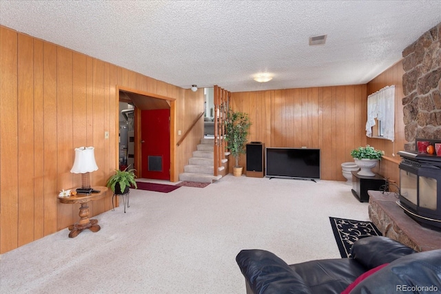 living area with water heater, a wood stove, carpet floors, wooden walls, and stairs