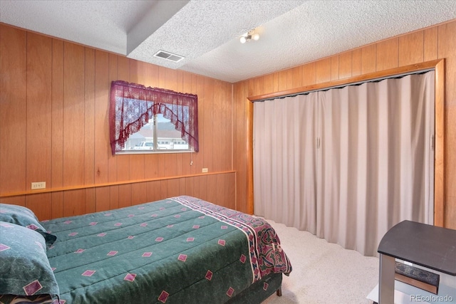 carpeted bedroom featuring a textured ceiling, wood walls, and visible vents