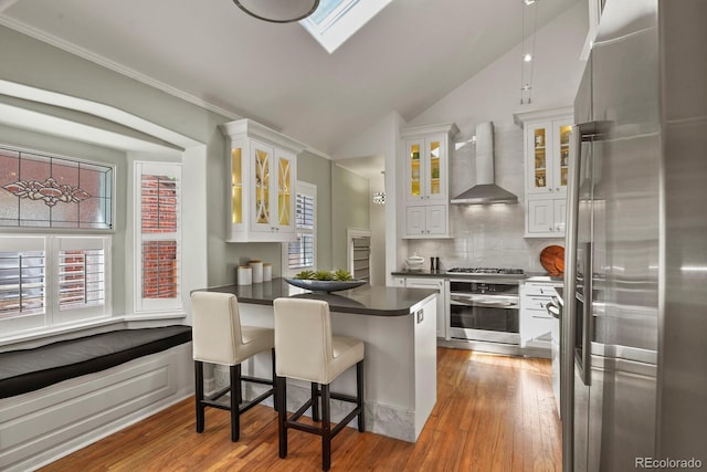 kitchen featuring appliances with stainless steel finishes, white cabinets, a kitchen bar, and wall chimney exhaust hood