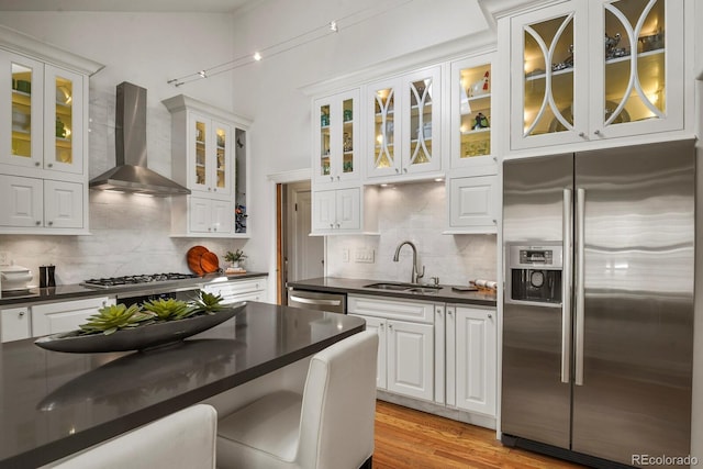 kitchen with appliances with stainless steel finishes, white cabinetry, sink, backsplash, and wall chimney exhaust hood