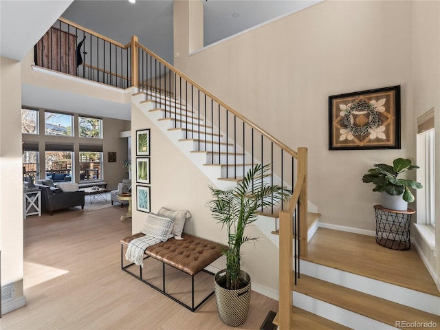 stairway featuring baseboards, a high ceiling, visible vents, and wood finished floors