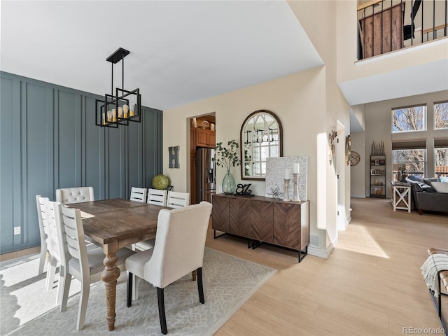 dining space with a chandelier, a high ceiling, a decorative wall, and light wood finished floors