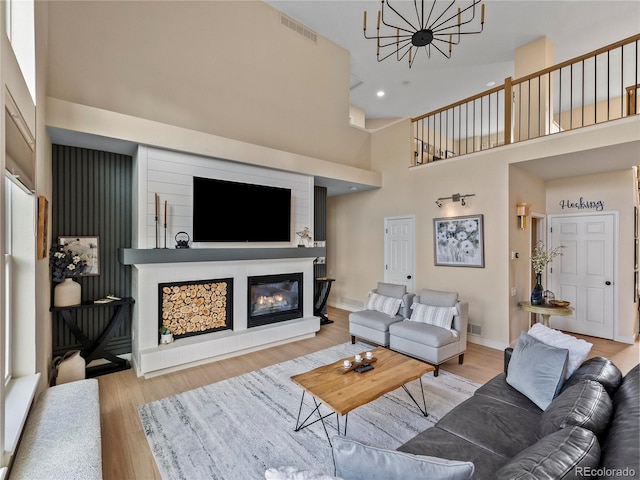 living area featuring visible vents, a high ceiling, a glass covered fireplace, wood finished floors, and baseboards