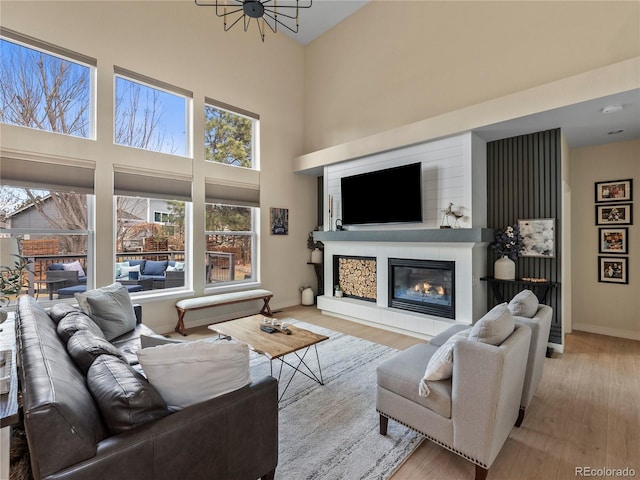 living room featuring a towering ceiling, baseboards, a tiled fireplace, and wood finished floors