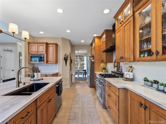 kitchen with appliances with stainless steel finishes, brown cabinets, a sink, and wall chimney exhaust hood