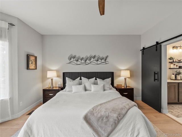 bedroom with a barn door, light wood-style flooring, and baseboards