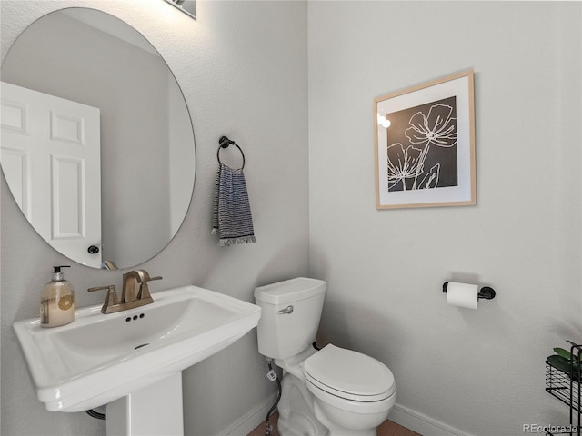 half bath featuring a sink, toilet, and baseboards