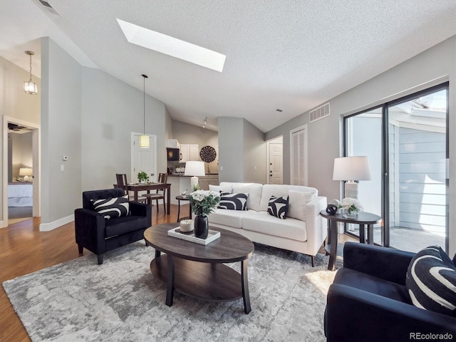 living area featuring wood finished floors, vaulted ceiling, a textured ceiling, baseboards, and a skylight