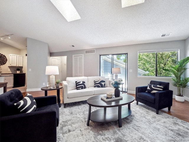 living room featuring light wood finished floors, a skylight, vaulted ceiling, a textured ceiling, and baseboards