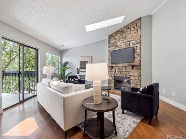 living area with a skylight, a textured ceiling, wood finished floors, a fireplace, and vaulted ceiling