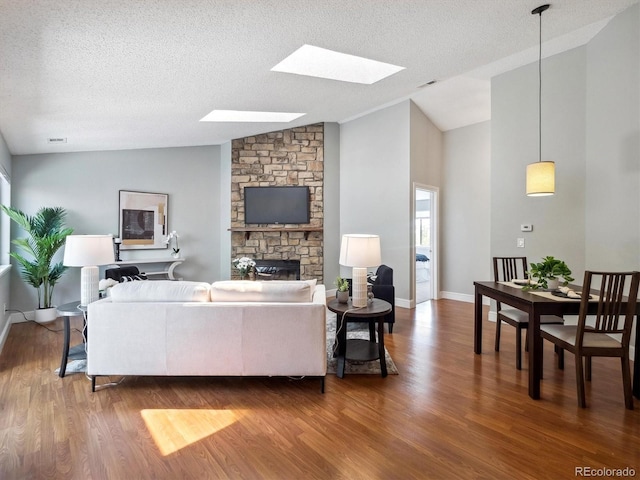 living area featuring vaulted ceiling, a skylight, wood finished floors, a textured ceiling, and a stone fireplace