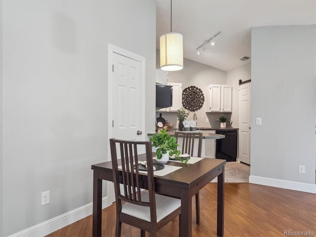 dining area with lofted ceiling, baseboards, rail lighting, wood finished floors, and a barn door