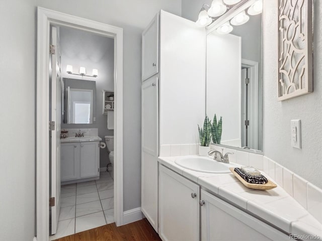 bathroom with toilet, two vanities, and baseboards