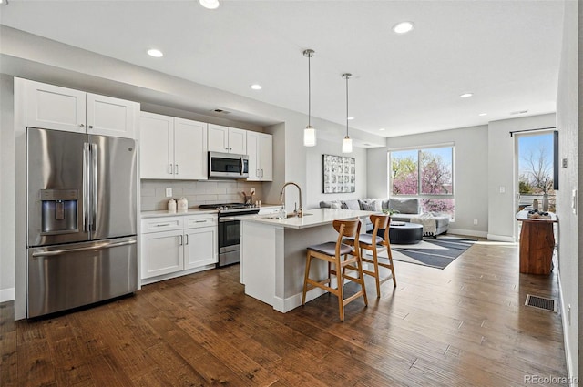 kitchen with visible vents, open floor plan, white cabinetry, a sink, and stainless steel appliances