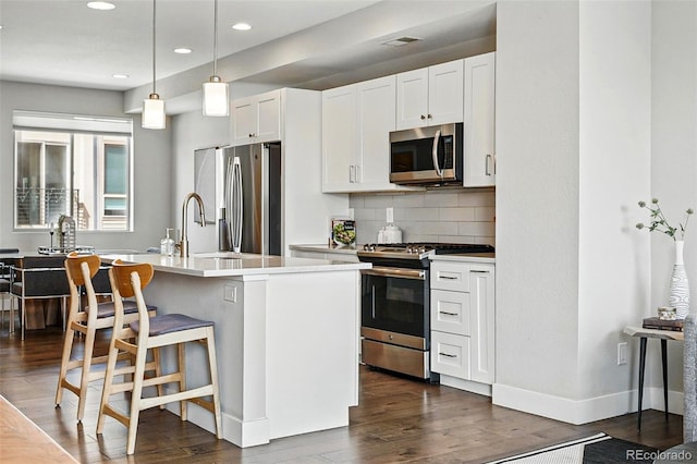 kitchen featuring backsplash, appliances with stainless steel finishes, dark wood finished floors, a sink, and a breakfast bar