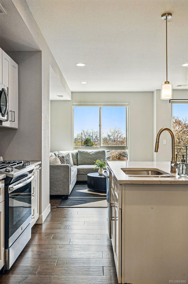 kitchen with pendant lighting, a sink, stainless steel appliances, white cabinetry, and dark wood-type flooring