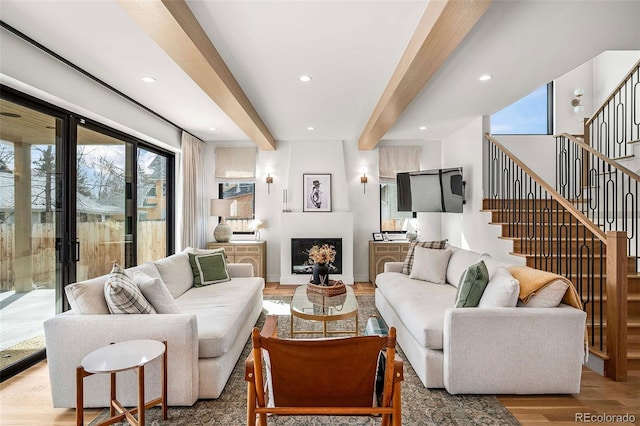 living room featuring stairs, beam ceiling, a fireplace, and wood finished floors