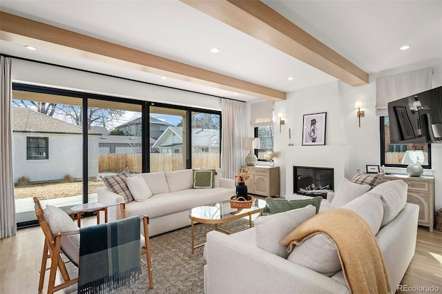 living room with light wood-type flooring, a glass covered fireplace, beamed ceiling, and recessed lighting