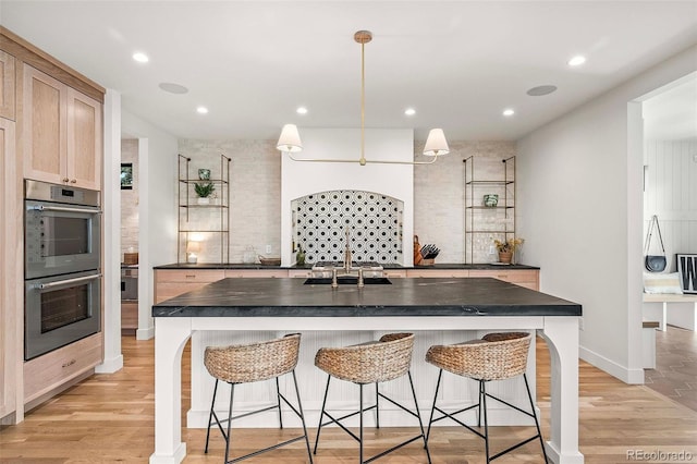 kitchen featuring double oven, dark countertops, a sink, and light wood-style flooring