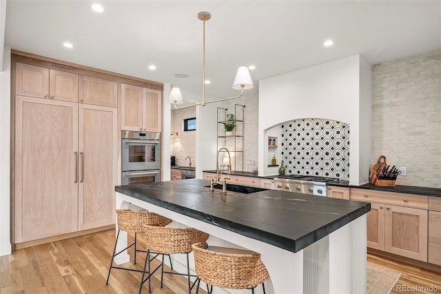 kitchen featuring dark countertops, light brown cabinets, stainless steel double oven, and a sink