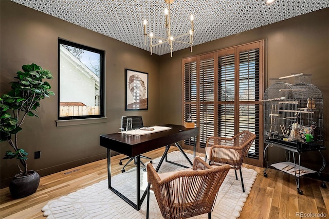 office featuring baseboards, visible vents, wood finished floors, a healthy amount of sunlight, and a notable chandelier