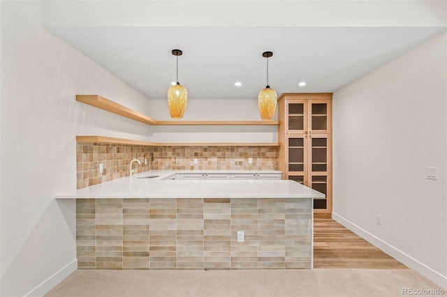 kitchen featuring decorative light fixtures, open shelves, light countertops, a sink, and a peninsula