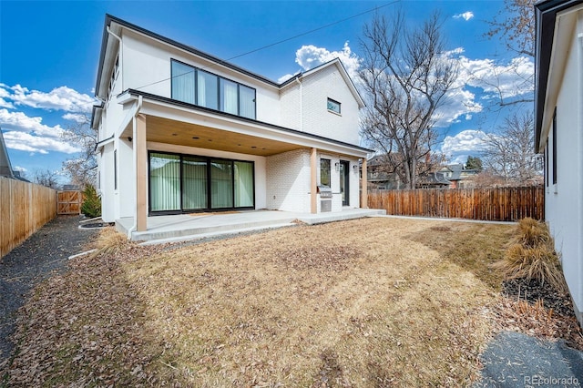 rear view of property with a fenced backyard, brick siding, and a patio