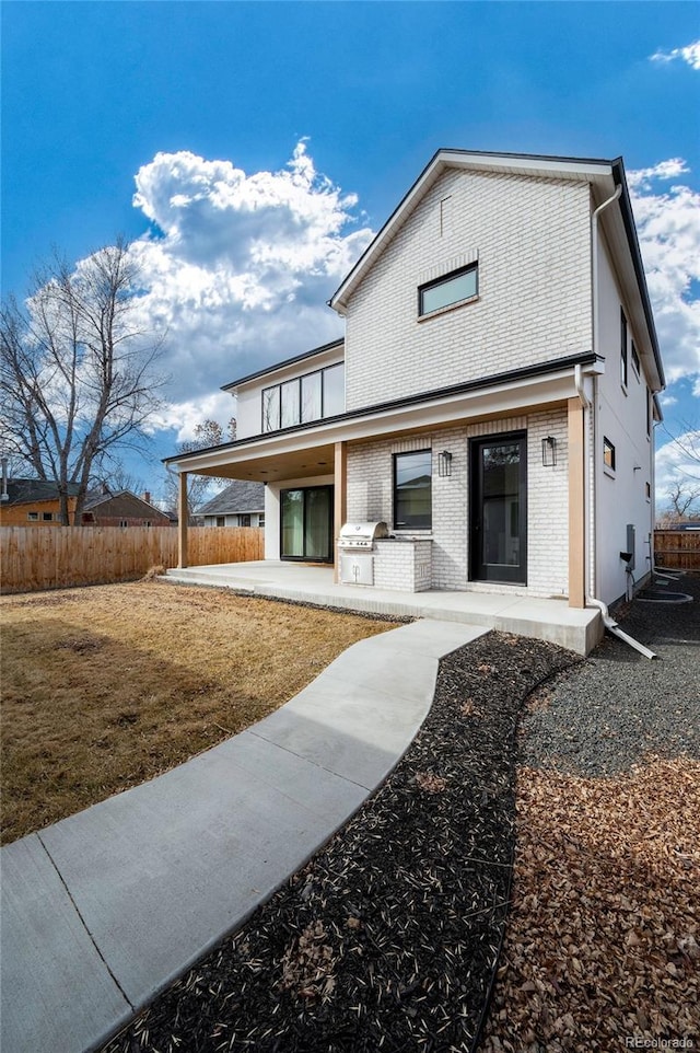 view of front of house with a patio, brick siding, and fence