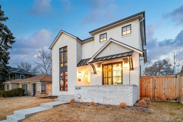 view of front of home with a standing seam roof, fence, metal roof, and brick siding