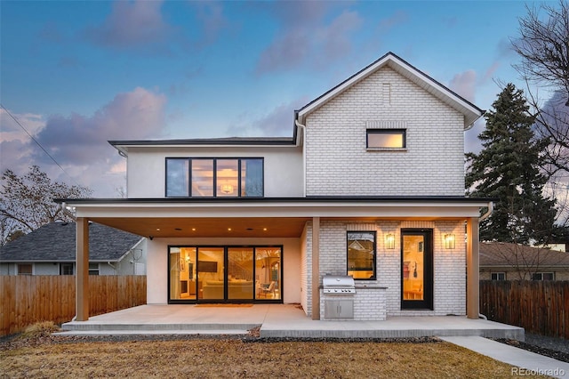 back of property at dusk featuring stucco siding, brick siding, a patio, and fence