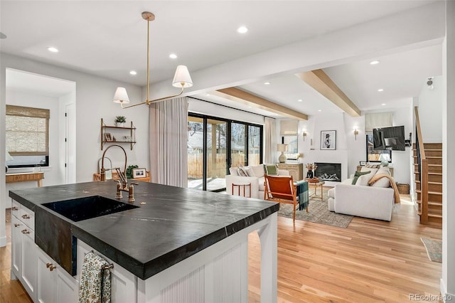 kitchen with dark countertops, a large fireplace, light wood-style flooring, and a sink