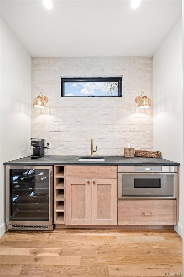 bar with wine cooler, light wood-style flooring, stainless steel oven, a sink, and wet bar