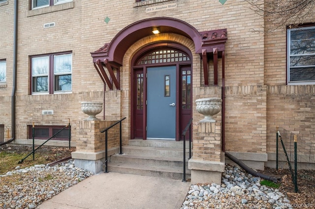 doorway to property featuring brick siding and fence