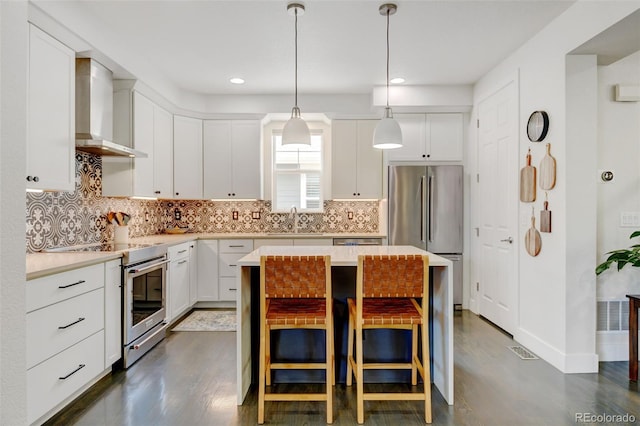 kitchen with wall chimney range hood, appliances with stainless steel finishes, dark wood finished floors, and a sink
