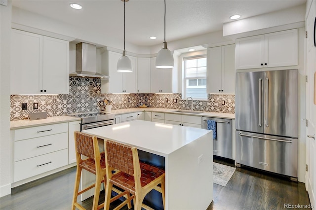 kitchen featuring dark wood-style floors, wall chimney range hood, a kitchen bar, a sink, and stainless steel appliances