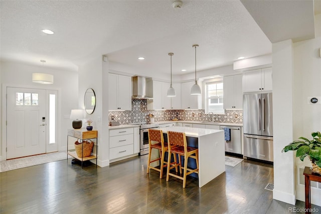 kitchen with wall chimney range hood, appliances with stainless steel finishes, a sink, a kitchen breakfast bar, and a kitchen island