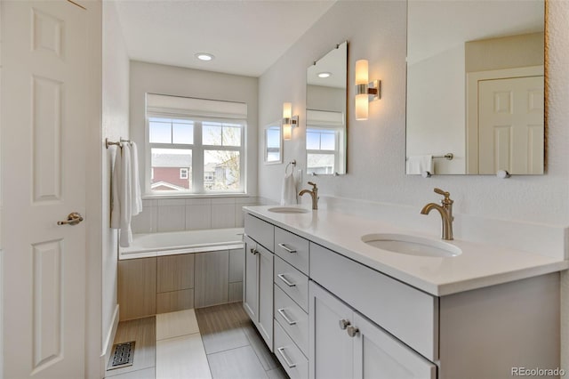 bathroom with double vanity, visible vents, a bathtub, and a sink