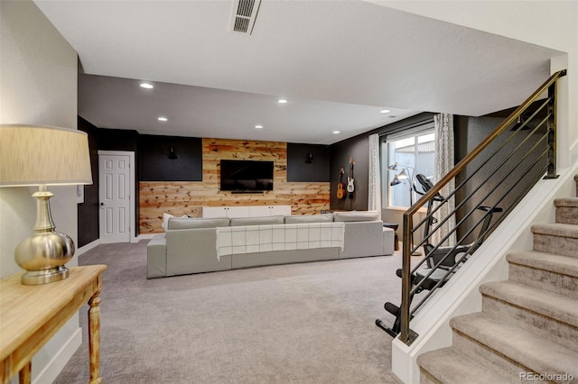 carpeted living room with visible vents, wood walls, stairs, an accent wall, and recessed lighting