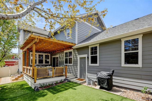 back of property with roof with shingles, a wooden deck, a yard, and fence