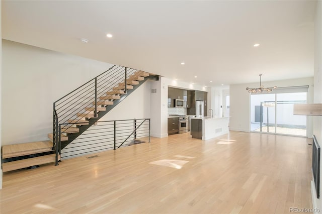 unfurnished living room with an inviting chandelier, sink, and light hardwood / wood-style flooring