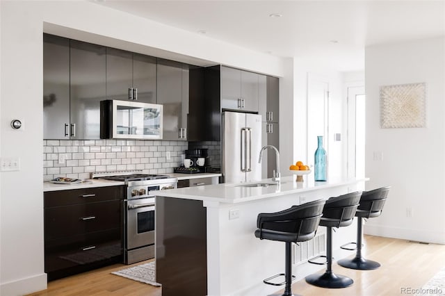 kitchen with sink, light hardwood / wood-style flooring, appliances with stainless steel finishes, backsplash, and a kitchen breakfast bar