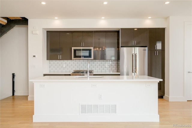 kitchen featuring an island with sink, appliances with stainless steel finishes, backsplash, and light hardwood / wood-style floors