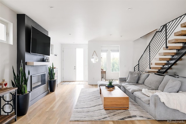 living room featuring light wood-style floors, a glass covered fireplace, and stairs