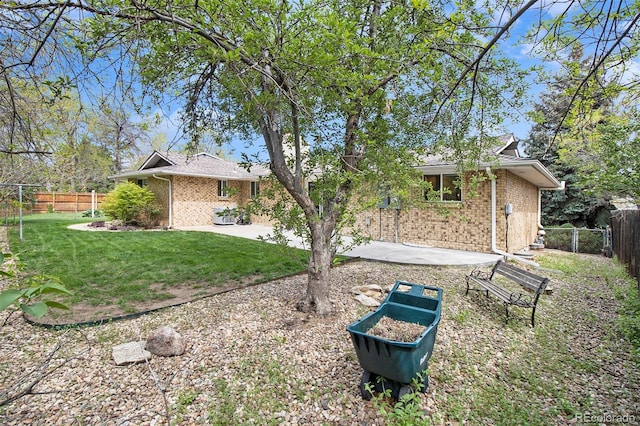 back of house with brick siding, a lawn, a fenced backyard, and a patio area