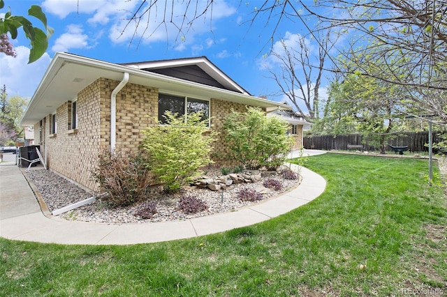 view of property exterior featuring brick siding, a yard, and fence