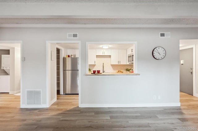 9700 E Iliff Ave Unit A3, Denver, CO 80231 - kitchen with stainless steel appliances, stacked washer and clothes dryer, white cabinetry, and light wood-type flooring